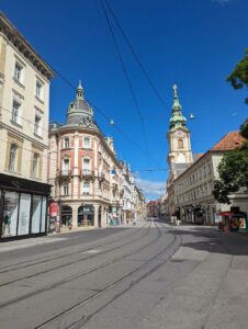 Main high street of a city. A tram line is visible and the sky is clear blue.