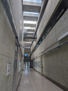 Long hallway of the interior of a concrete building. The wallway extends through all floors and the sky is visible.