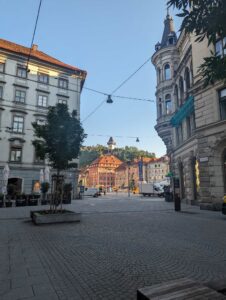 View of a city square. A small clocktower can be seen at the top of a hill in the background.