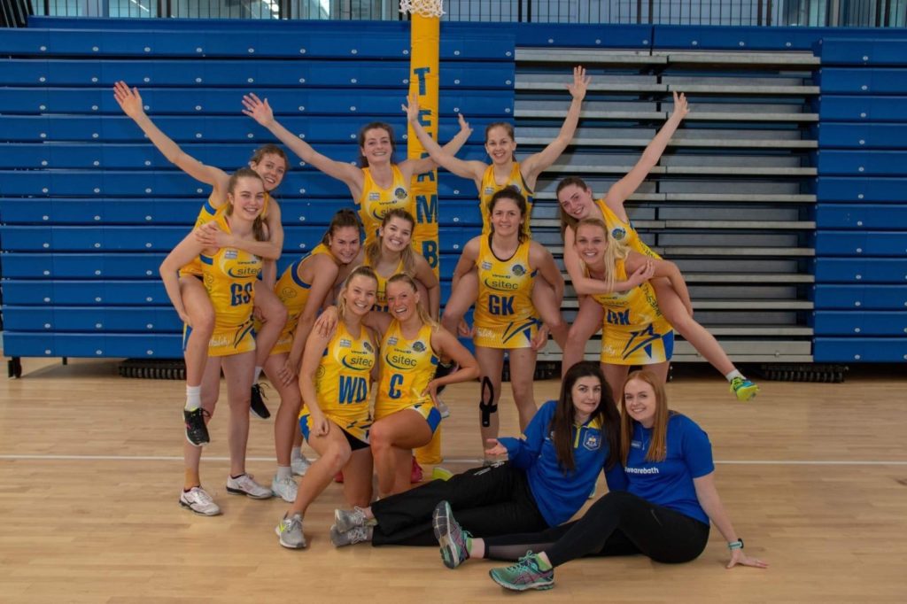 A group shot of the University of Bath netball players in their netball kit celebrating at a cup final