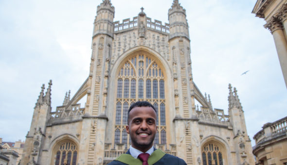 Jonathan in his graduation gown (with green neckline) in a navy blue suit and burgundy tie stood in front of Bath Abbey.