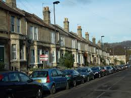 A row of houses in the Oldfield Park area of Bath with some cars parked outside. There is a purple and white For Sale board outside one of the properties.