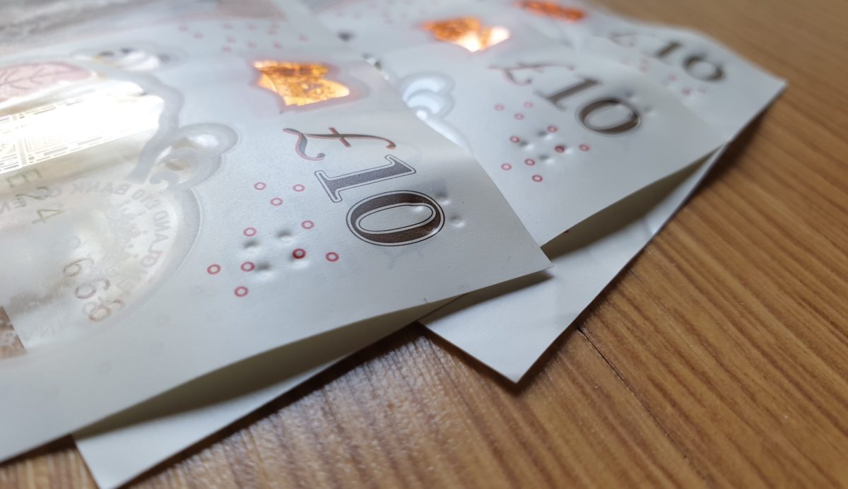 Three £10 notes ( particial not whole) on a wooden table