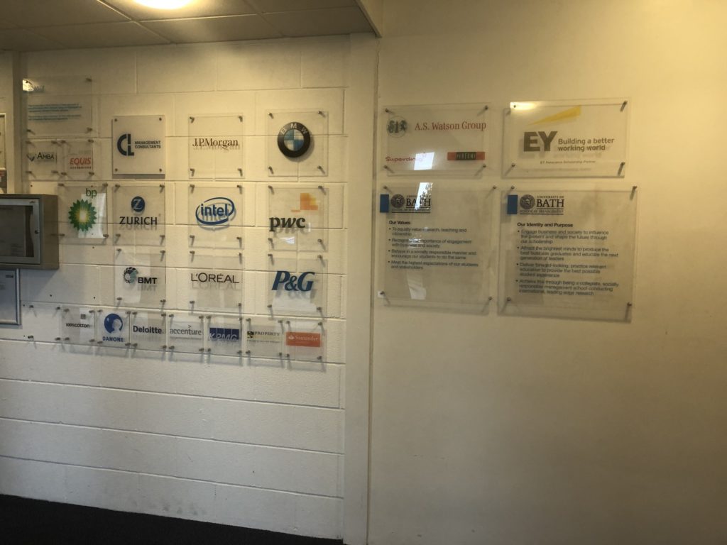 The foyer of the School of Managment where there are numerous glass company plaques on a white wall. The plaques include the company's name and their logo.