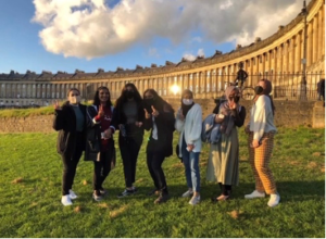 Seven people are standing in front of the Royal Crescent, which is a row of terraced houses laid in a curved shape.
