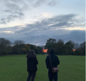Two people are standing in a park and watching the sun set.
