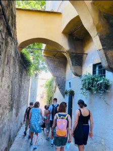 A group of people wearing backpacks walking down a narrow cobbled street.