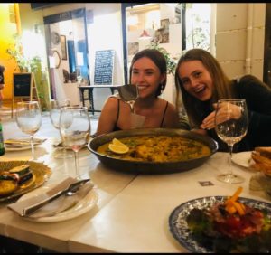 Two young women with a big pan of paella in a restaurant.