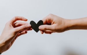 Two hands holding a black paper heart. 