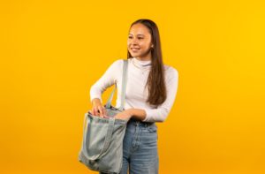 Female student posed in front of yellow screen taking file out of shoulder bag.