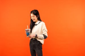 Female student posed in front of orange screen holding soft drink.