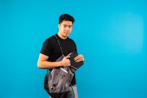 Male student posed in front of blue screen taking file out of shoulder bag.