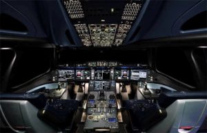 The view of the inside of an Airbus A350 family cockpit at night. The buttons, switches, screens and dials are lit up in electric neon against the coal blackness of the console around them.