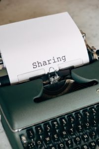 A typewritter with the words "sharing" written. The type writer is dark green with black keys. 