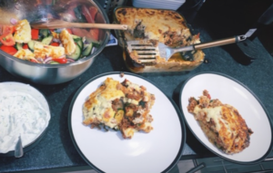 A baking tray containing mousaka bake, a salad bowl with a greek salad and two plates are on a kitchen counter top.