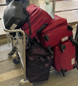 A picture containing two red check-in bags, one purple duffel check-in bag, one cabin bag, and black one laptop bag.