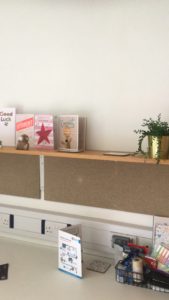 Pin boards and shelf with a small green plant and cards on it. The desk below has a desk tidy and a card