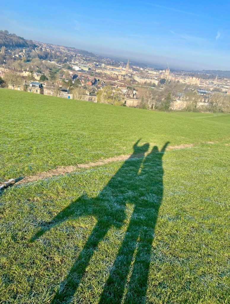 Two shadows on a green hill overlooking the skyline of the city of Bath