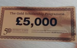 A shiny, gold ticket, and displayed in black and bold is '£5,000', with some other text written underneath the bold writing.