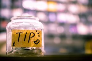 A jar with a yellow post-it note on the front saying tip, the background is blurred out