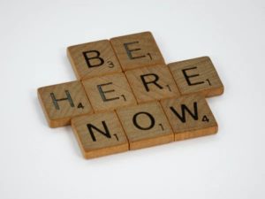 Scrabble text saying "be here now"