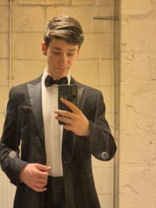 Ben taking a photo in a mirror whilst wearing a suit. 