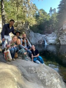 Six people (Nell and friends) posing on a large rock, next to a lake with a waterfall in the background