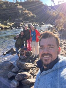 Selfie of 4 people (Nell and friends) in front of a scenic stream of water and hillside