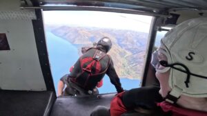 View of a person's back, in skydiving gear, as they lean out of an aeroplane
