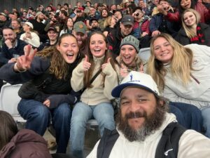 Selfie of 5 people (Grace and friends) sat amongst a crowd of people