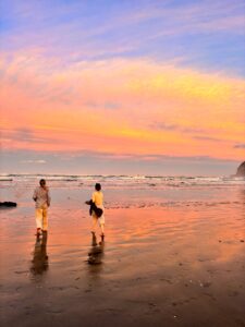 Two people walking on a sandy beach during a sunset