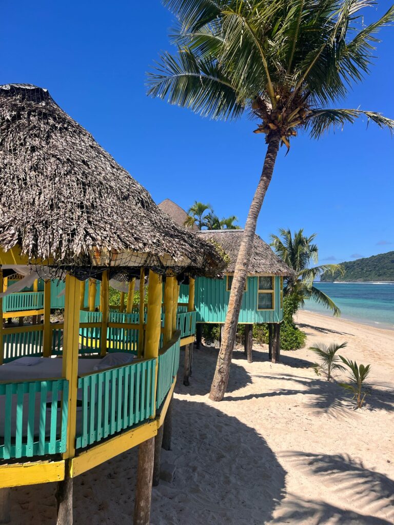 Two wooden huts with thatched roofs on a sandy beach
