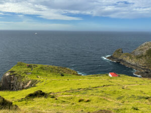 View of a grass field and cliff face in the foreground, leading into the ocean in the background.