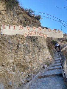 Rocky steps alongside a hill, with a wooden sign above it that reads: 'Bienvenidos a San Isidro'