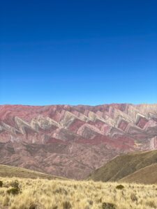 A purple-tinted mountain range against a clear blue sky. The mountains are the ‘la sierra de catorce colores’, The Mountain of Fourteen Colours