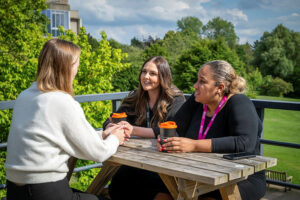 Three people sitting at a table outside chatting